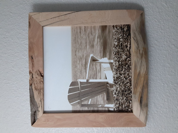 Back of simple wood beach chair, sitting on beach stones.  Sepia print on canvass.  Natural edge alligator juniper frame.